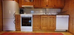 Eine Küche mit Holzschränken, einem weißen Herd, einem weißen Kühlschrank und einem roten Teppich.