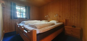 Ein Zimmer mit Holzboden, einem Bett, zwei Nachttischen und einem Fenster mit Vorhängen.