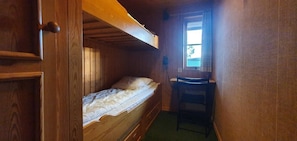 Ein kleiner, hölzerner Raum mit einem Etagenbett, einem Schreibtisch und einem Fenster.