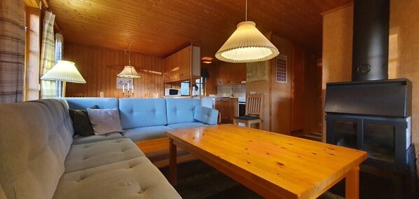 Ein gemütliches Blockhauss-Interieur mit einer Couch, einem Holzesstisch, Pendelleuchten und einem Kamin.