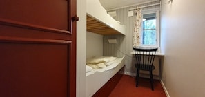 Ein schmaler Raum mit einem Etagenbett, einem kleinen Tisch und einem Stuhl.