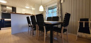 Ein Essbereich mit Tisch und Stühlen, ein Fenster mit Vorhängen sowie eine Küche im Hintergrund.