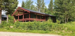 Eine Holzhütte mit Veranda, umgeben von dichtem Grün und Bäumen.