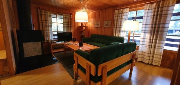 A wooden interior with a green sofa, a wooden table, a fireplace, and plaid curtains. - Sauna | Wi-Fi | Terrace | Wood stove | Cable TV (Lofsdalen)