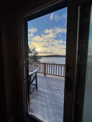 Vista através de uma porta para um deck com guarda-corpo, um banco e uma paisagem coberta de neve.
