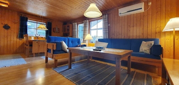 A wooden interior with a blue sofa, a wooden table, and a dining area.