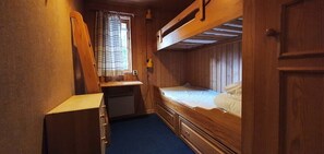 A compact cabin with bunk beds, a small desk, and a window with curtains.