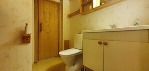 A bathroom with a toilet, wooden door, and a cabinet with a mirror above it.