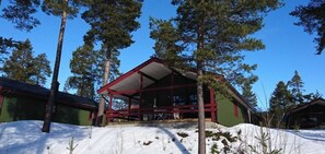 Eine Hütte mit rotem Dach und überdachter Veranda, umgeben von Schnee und hohen Kiefern.