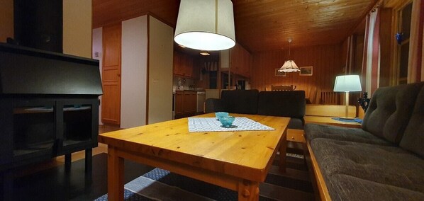Ein Holztisch mit Untersetzer und einem blauen Glas, ein Sofa, eine Lampe sowie eine Küchenzeile.