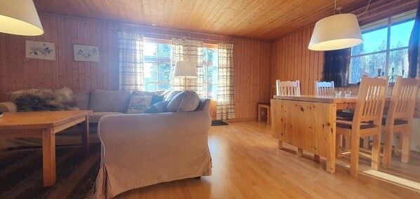 Ein Holzinnenraum mit einer Couch, einem Esstisch, Stühlen und einem Fenster mit Vorhängen.