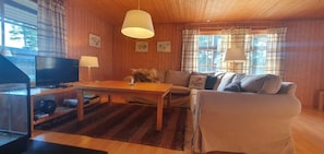 Ein gemütliches Blockhausschlafzimmer mit einem Holzespeise-Tisch, einer Couch, einem Fernseher und einem Fenster mit Vorhängen.