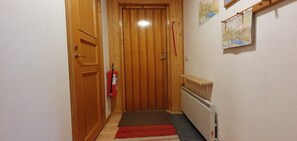 Ein Flur mit einer Holztür, einem Feuerlöscher, einer Heizung und einem kleinen Regal.