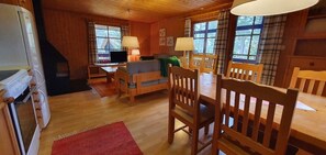 Ein Holzblockhaus-Interieur mit Esstisch, Stühlen, einer Couch, einem Fernseher und einem Kamin.