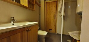 Ein Badezimmer mit einem Holzbadezimmermöbel, einem weißen Waschbecken, einer Toilette und einer Duschkabine.