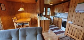 Ein Holzinnenraum mit Esstisch, Stühlen, einer Couch, einer Küche mit Holzschränken und einem Kühlschrank.