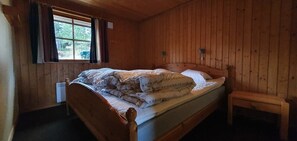 Ein Zimmer mit Holzwänden, einem Bett, einem Fenster und einer Bank.