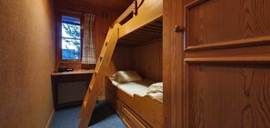 Ein Stockbett mit Schreibtisch und Fenster, Holzwände und Blick auf Bäume.