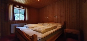 Ein Zimmer in einer Holzhütte mit einem Bett, einem Fenster mit Vorhängen und einer kleinen Bank.