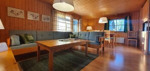Ein Interieur einer Holzhütte mit einer Couch, einem Esstisch, Stühlen und Bildern an den Wänden.
