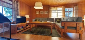 Ein Holzinnenraum mit Sofa, Tisch, Fernseher und Vorhängen.