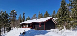 Eine Hütte mit schneebedecktem Dach, umgeben von Bäumen, und einem strahlend blauen Himmel.