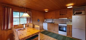 Ein Holzblockhaus-Interieur mit Esstisch, Stühlen, einer Küche inklusive Herd, Backofen und Kühlschrank.