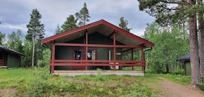 A cabin with a red roof and a porch, surrounded by trees.