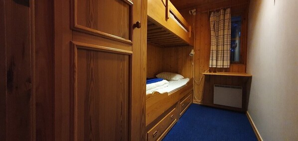Habitación pequeña con literas, un escritorio y una ventana con cortinas.