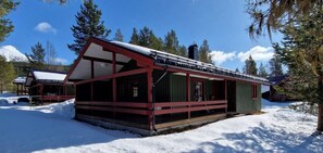 Eine Holzhütte mit Metalldach, umgeben von Schnee und Bäumen.