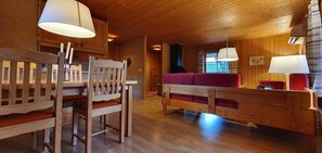 Ein Holzinterieur mit Esstisch, Stühlen, einer Couch und Lampen.