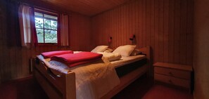 Ein Zimmer mit Holzboden, einem Bett, einem Nachttisch und einem Fenster mit Vorhängen.