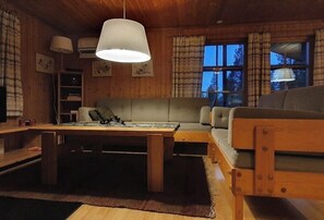 Ein gemütliches Blockhauss-Interieur mit Holztisch, Sofa und einer Pendelleuchte.
