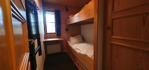 Ein schmales Kabinett mit einem Etagenbett, einem kleinen Schreibtisch und einem Fenster mit Vorhängen.