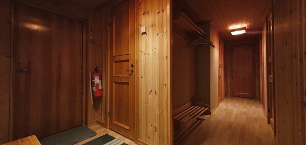 A wooden interior hallway with a fire extinguisher, a door, and a staircase.