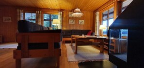 Ein gemütliches Blockhauss-Interieur mit Holzbalkendecke, einer Couch, einem Tisch und einem Fenster mit Vorhängen.