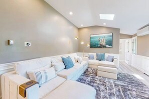 Een moderne woonkamer met een hoekbank, een schilderij van een zeilboot, inbouwspots en een marmeren vloer.