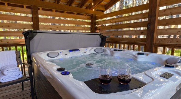 Ein Whirlpool mit zwei Gläsern Rotwein, einem Handtuch und einer Holzterrasse.