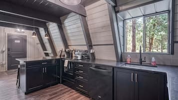Une cuisine moderne avec des meubles de couleur sombre, un îlot central et une grande fenêtre donnant sur la forêt.