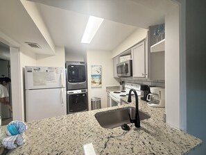 Eine Küche mit Granit Arbeitsplatte, Spüle aus Edelstahl, Mikrowelle, Herd und Kühlschrank.