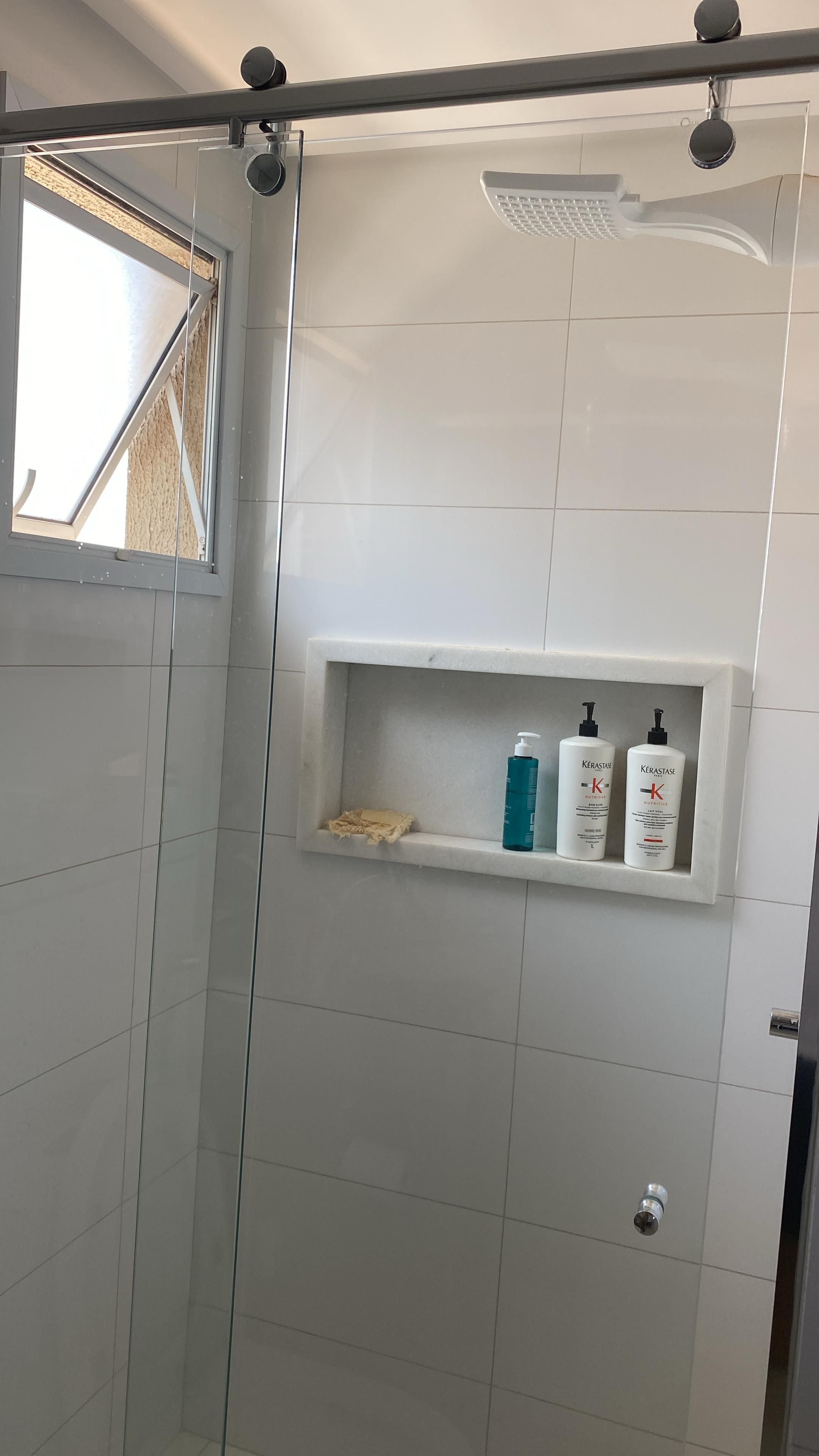 Bruseområde med glasdør, hylde med toiletartikler og brusehoved monteret i loftet.