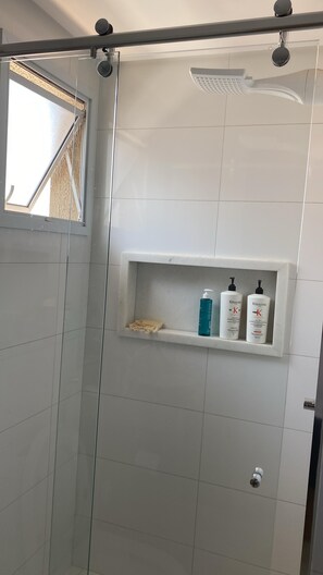 A shower area with a glass door, a shelf with toiletries, and a ceiling-mounted showerhead. - Deluxe Room 2 (Foz do Iguaçu)