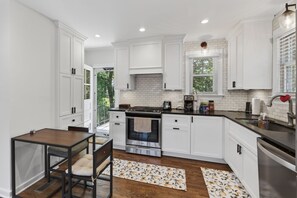 Eine moderne Küche mit weißen Schränken, einem eingebauten Backofen und einem Essbereich mit Holztisch und -stühlen.
