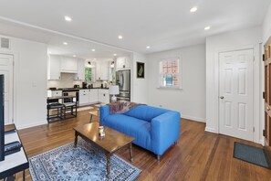 Ein modernes Wohnzimmer mit einem blauen Sofa, einem Holztisch und einer Küche im Hintergrund.