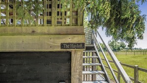 Un bâtiment en bois avec une enseigne indiquant « The Hayloft », un escalier menant à une terrasse et un espace extérieur clôturé.