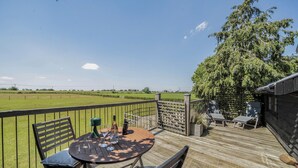 Une terrasse en bois avec une table et des chaises, une vue sur un champ verdoyant et un grand arbre.