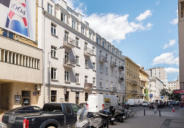 Eine Straße mit parkenden Fahrzeugen, ein Gebäude mit Balkonen und einem klaren Himmel.