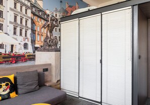 A room with a sofa, a large window with blinds, a statue, and a view of buildings and a train. - Warsaw Art Studio III with Mezzanine (Warszawa)