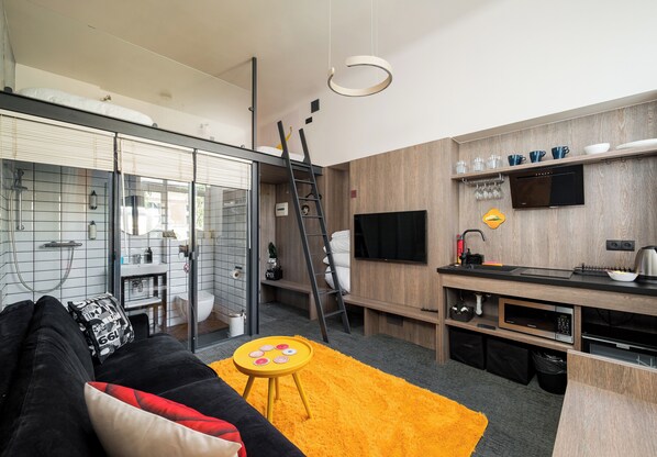 A compact living space with a kitchenette, a sofa, a small round table, a TV, and a ladder. - Warsaw Art Studio IV with Mezzanine (Warszawa)