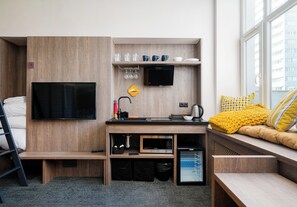 A compact hotel room with a kitchenette, a flat-screen TV, a sofa with yellow cushions, and a window with a city view. - Warsaw Art Studio IV with Mezzanine (Warszawa)